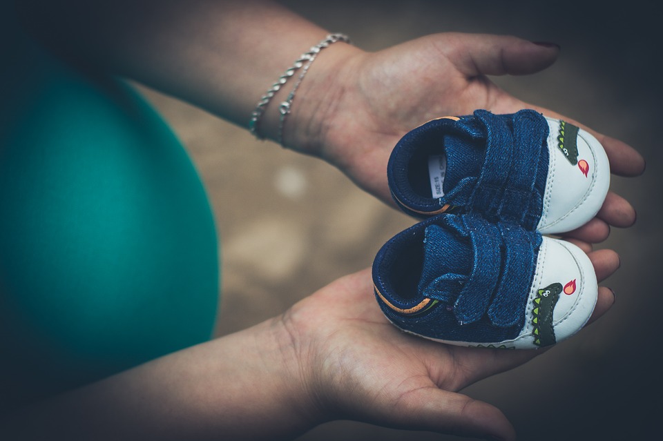 image d'une maman enceinte tenent dans sa main des chaussures pour bébé